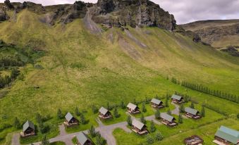 a mountainous landscape with a group of small wooden cabins , situated on grassy hillsides under a cloudy sky at Hörgsland Cottages