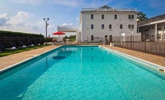 a swimming pool with a white building in the background and red umbrellas in front of it at Best Western White House Inn