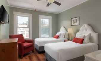 a hotel room with two twin beds , a red chair , and a ceiling fan , all decorated in white and gray colors at Thayers Inn