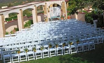 a large outdoor wedding venue with rows of white chairs arranged in an open area , ready for guests at Dream Manor Inn