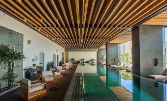 a modern , well - lit indoor swimming pool area with wooden decking , greenery , and comfortable seating arrangements at Hyatt Regency Andares Guadalajara