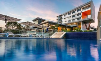a modern hotel with a large swimming pool , umbrellas , and outdoor seating areas under a clear blue sky at Acantilados