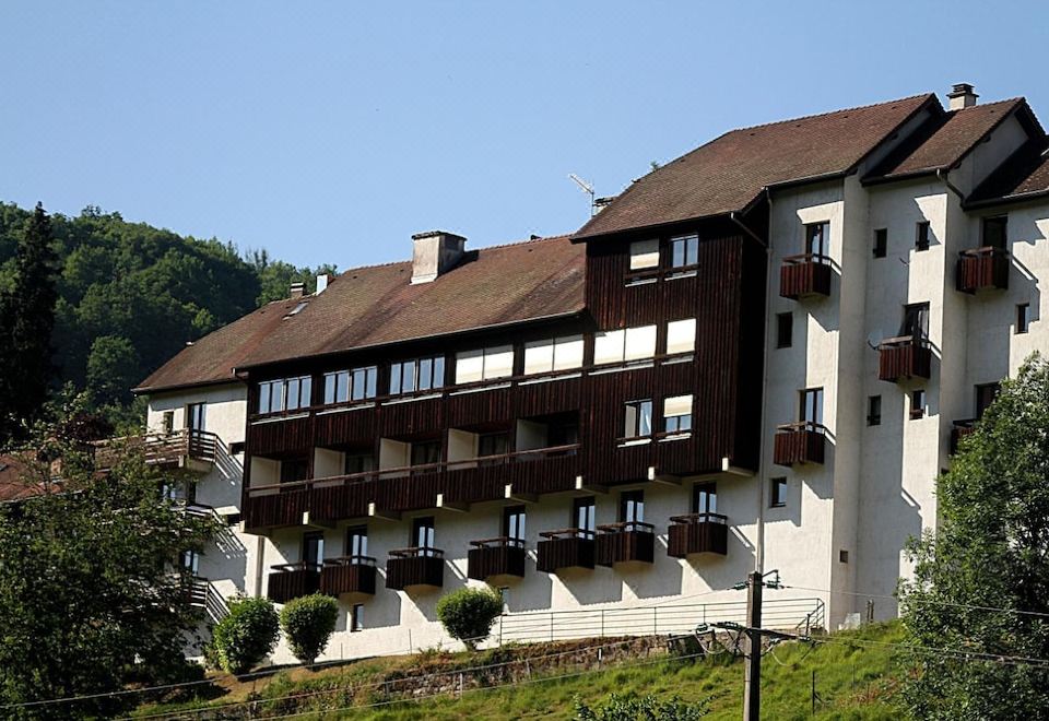 a large , two - story building with multiple balconies and windows , situated on a hillside with trees and shrubs in the background at La Cascade