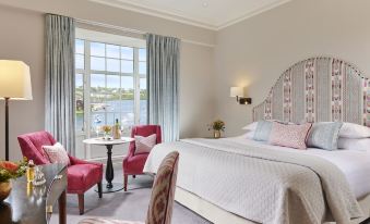 a large bed with a white comforter and pink pillows is in the middle of a room with pink chairs at Actons Hotel Kinsale