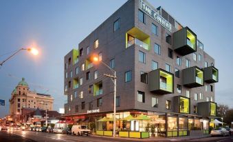 a modern building with yellow and green balconies is situated on a street corner at dusk at The Cullen Melbourne - Art Series