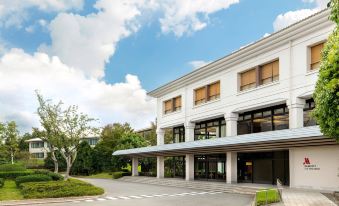 a modern , white building with a large glass window and a blue roof , surrounded by trees and grass , under a partly cloudy sky at Izu Marriott Hotel Shuzenji