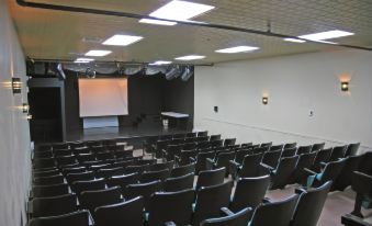 a large , empty auditorium with rows of black chairs arranged in a symmetrical fashion , and a projector screen on the wall at Chateau Madelinot