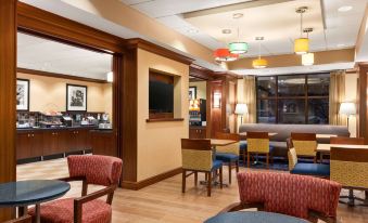 a well - lit hotel lobby with various seating options , including couches and chairs , as well as a dining area at Hampton Inn Warrenton