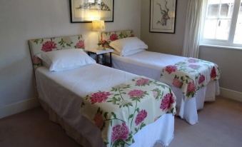 a bedroom with two beds , each adorned with floral bedspreads and pillows , flanked by nightstands and framed pictures on the walls at Moor Court Farm