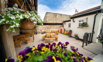 a courtyard with a stone wall , wooden tables and chairs , and hanging planters filled with flowers at The Oddfellows Arms