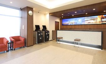 The lobby features a reception desk, a seating area, and a wall displaying information at AB Hotel Kisarazu