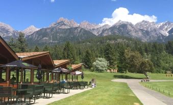 a picnic area with benches and umbrellas , surrounded by trees and mountains , under a clear blue sky at Fairmont Hot Springs Resort