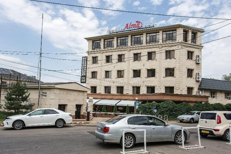 "a large white hotel building with the name "" alvor "" prominently displayed on its sign , surrounded by cars parked in front of it" at Alma