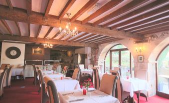 a large dining room with wooden beams on the ceiling , white tablecloths on the tables , and chairs arranged for a meal at The Crown Hotel