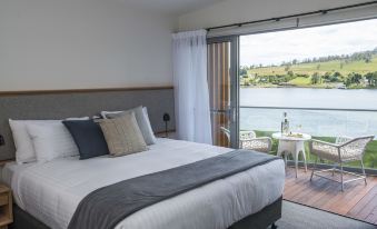 a large bed with a gray headboard is in a room with a window overlooking a lake at Rosevears Riverview Hotel