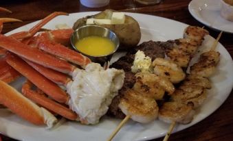 a dining table with a variety of seafood , including lobster , shrimp , and steak , served on a white plate at RiverBend Lodge