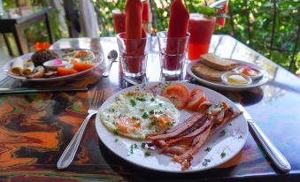 a plate of breakfast food , including eggs , bacon , and tomatoes , is placed on a table with other dishes and drinks at Conchal Hotel