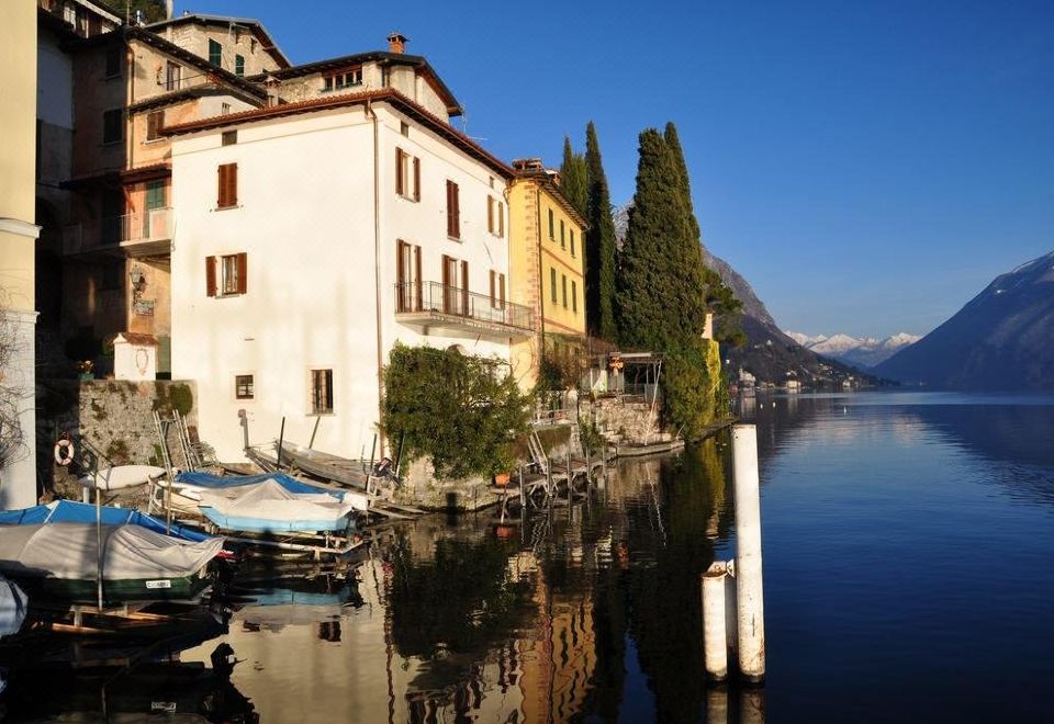 a row of houses and boats on a body of water , with mountains in the background at Hotel Stella d'Italia
