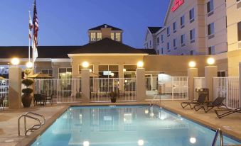an outdoor swimming pool surrounded by a hotel , with people enjoying their time in the pool area at Hilton Garden Inn Clovis