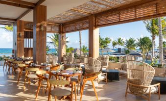a restaurant with wooden tables and chairs , surrounded by palm trees and a view of the ocean at Fairmont Mayakoba