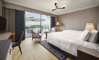 a spacious bedroom with a king - sized bed , a large window overlooking the ocean , and various pieces of furniture at Kawana Hotel