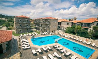 a large swimming pool surrounded by multiple buildings , with lounge chairs and umbrellas placed around the pool area at Royal Hotel and Suites