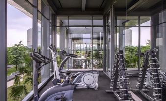 a well - equipped gym with various exercise equipment , including treadmills and weight machines , under large windows at Mercure Tangerang BSD City