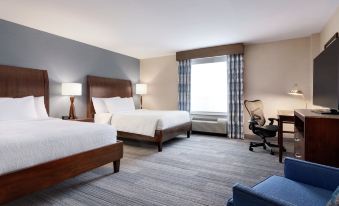 a hotel room with two beds , a desk , and a window , all decorated in neutral colors at Hilton Garden Inn Stony Brook