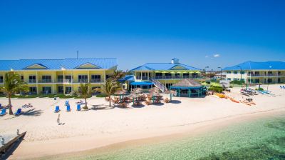 a tropical beach resort with multiple buildings and umbrellas on the sandy shore , under a clear blue sky at Wyndham Reef Resort Grand Cayman