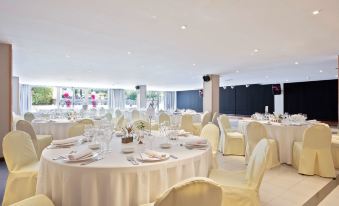 a large , well - lit dining room with round tables covered in white tablecloths and adorned with elegant decorations at Sol Costa Daurada