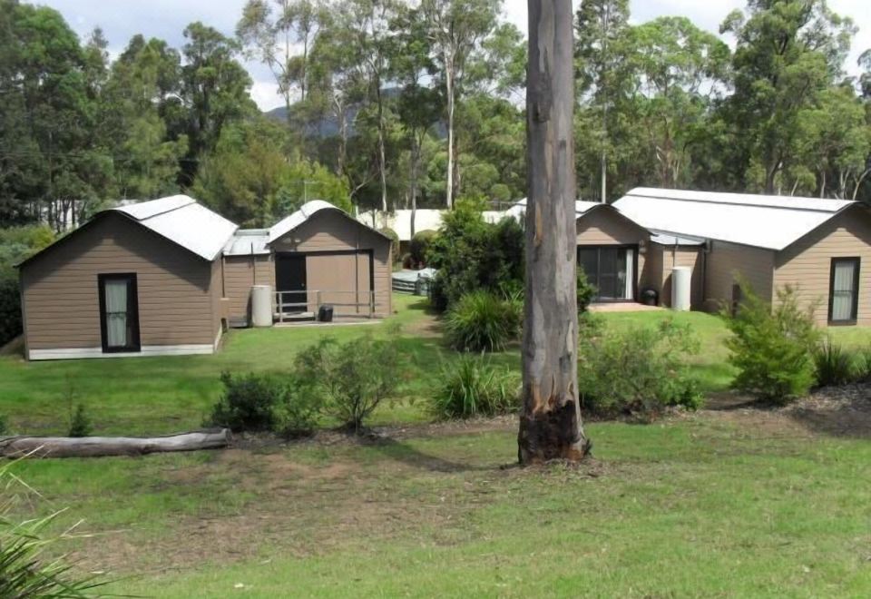 a group of small wooden houses surrounded by a grassy field , with trees in the background at Hunter Valley Retreat