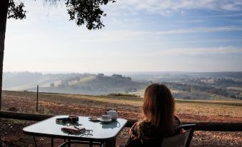 a woman is sitting at a table on a patio , enjoying the view of the countryside at Balingup Heights Hilltop Forest Cottages