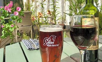 a glass of beer and a wine glass are placed on a wooden table , accompanied by a bottle of wine at Sibton White Horse Inn