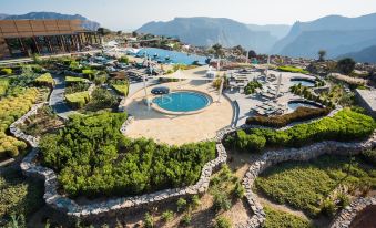 a large outdoor pool surrounded by lush greenery and mountains , with several lounge chairs and umbrellas placed around the pool area at Anantara Al Jabal Al Akhdar Resort