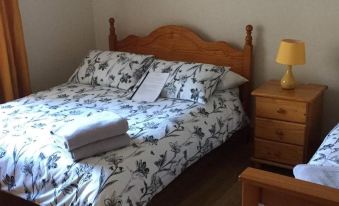 a neatly made bed with white and black floral bedding , a wooden headboard , and a nightstand beside it at Tara House
