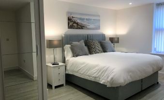 a large bed with white linens and a gray headboard is in a bedroom with wooden floors at Ice House Apartments