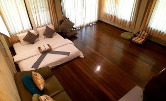 a large bedroom with hardwood floors , a large bed , and several pieces of furniture such as a couch , chairs , and a television at BaanSuanLeelawadee Resort Amphawa