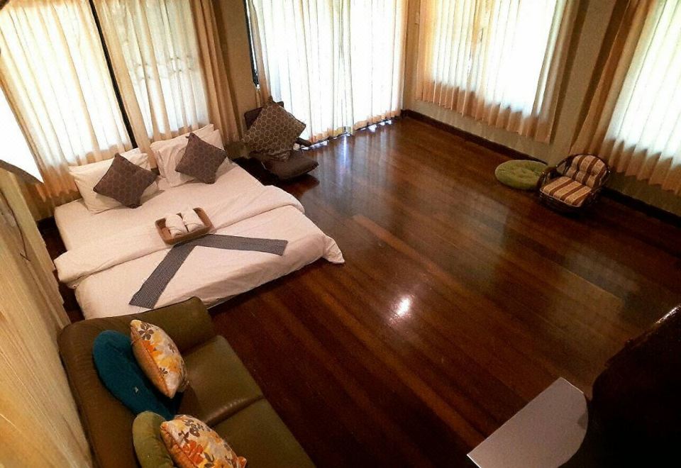 a large bedroom with hardwood floors , a large bed , and several pieces of furniture such as a couch , chairs , and a television at BaanSuanLeelawadee Resort Amphawa