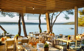 an outdoor dining area at a restaurant overlooking a body of water , with several tables and chairs arranged for guests at Lanterna Premium Camping Resort by Valamar