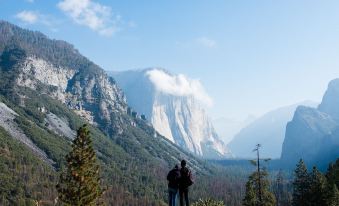 a man and a woman are standing on a hillside , looking out over a mountain range at AutoCamp Yosemite