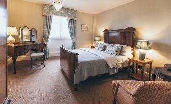 a large bed with a wooden headboard is in the center of a room with a chair , dresser , and window at Rowton Castle