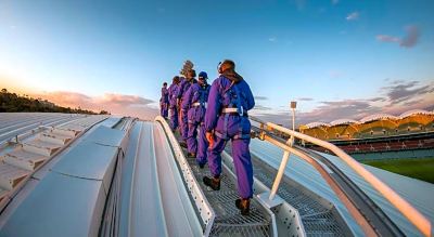 a group of men wearing blue overalls and hard hats are walking on a metal walkway at Oval Hotel at Adelaide Oval, an EVT hotel