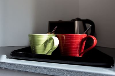 a pair of green and red mugs with spoons in them are placed on a tray at Village Hotel Liverpool
