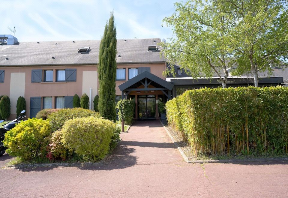 a building with a stone pathway leading to it , surrounded by greenery and trees , under a clear blue sky at Best Western the Hotel Versailles