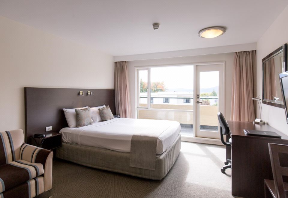 a modern hotel room with a large bed , white bedding , and sliding glass doors leading to a balcony at St Ives Apartments