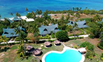 aerial view of a tropical resort with multiple thatched - roof buildings , a swimming pool , and palm trees near the ocean at Badian Island Wellness Resort