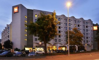 a city street at dusk , with a tall building in the background and several cars parked on the street at Ibis Strasbourg Centre Historique