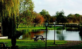 a grassy field with a picnic table and benches , surrounded by trees and a lake in the background at Queens Head Inn