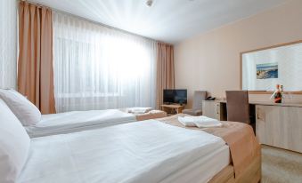 a hotel room with two beds , a desk , and a window , all neatly arranged in a minimalist style at Millennium Spa