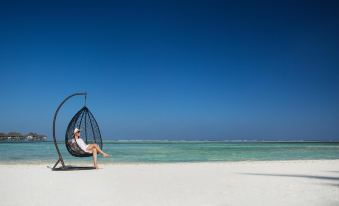 a woman is sitting in a black wicker chair on a white sandy beach , enjoying the sunny day at Pearl Sands of Maldives